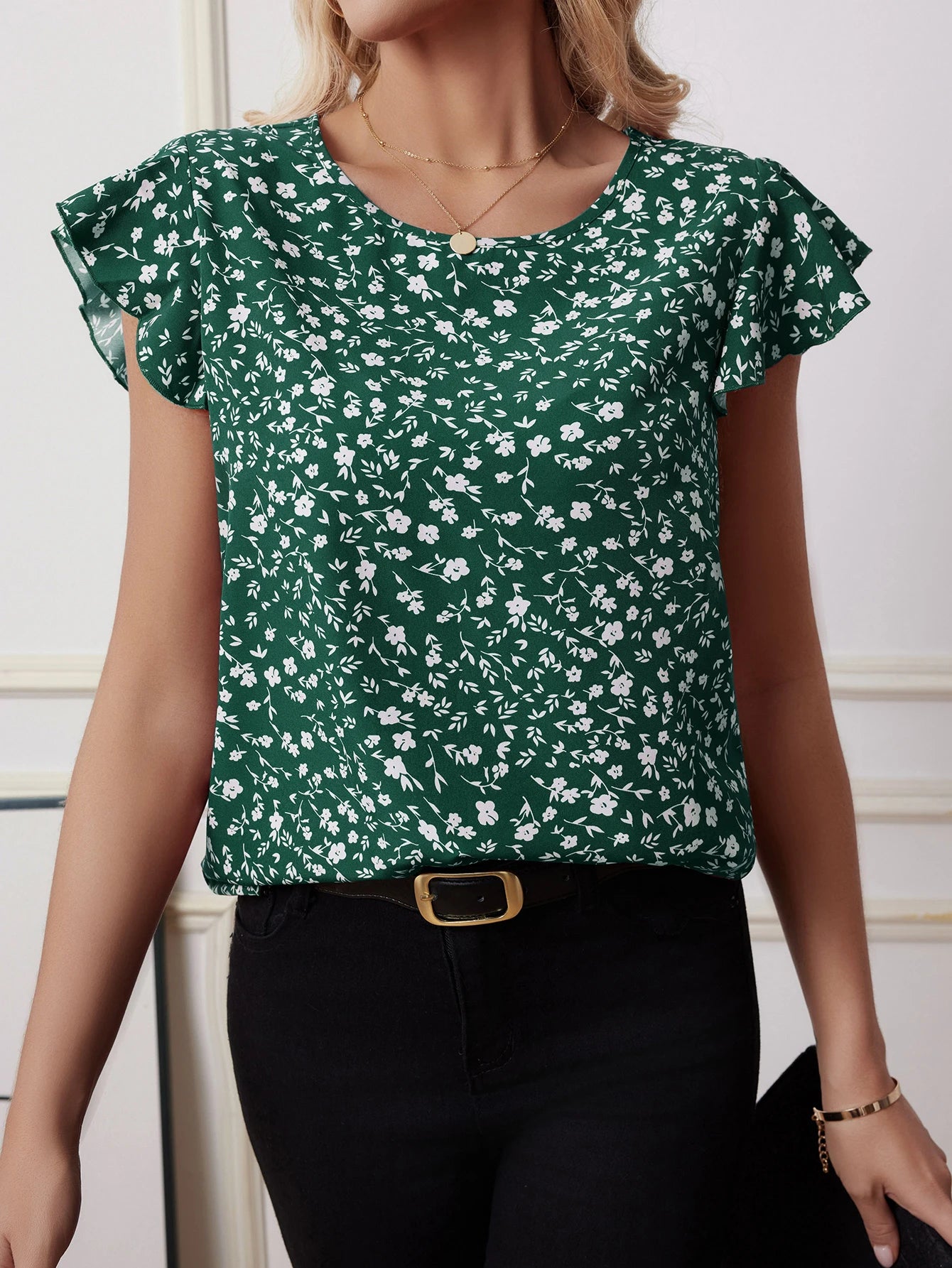 Woman in green boho floral blouse with white flower print and butterfly sleeves, styled with black jeans for a fresh spring-summer look.